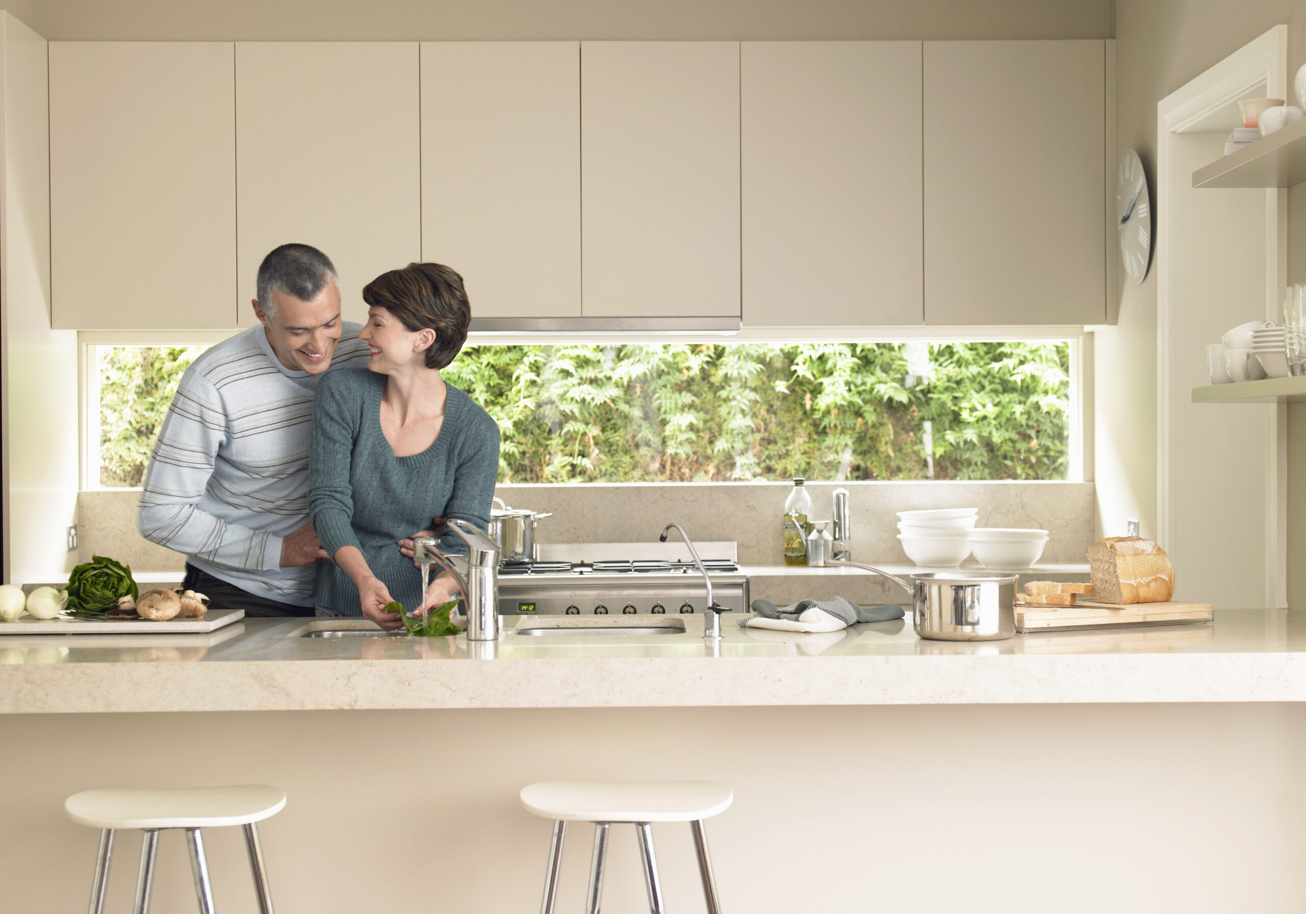 Happy,Woman,Washing,Vegetables,While,Man,Hugging,Her,From,Behind